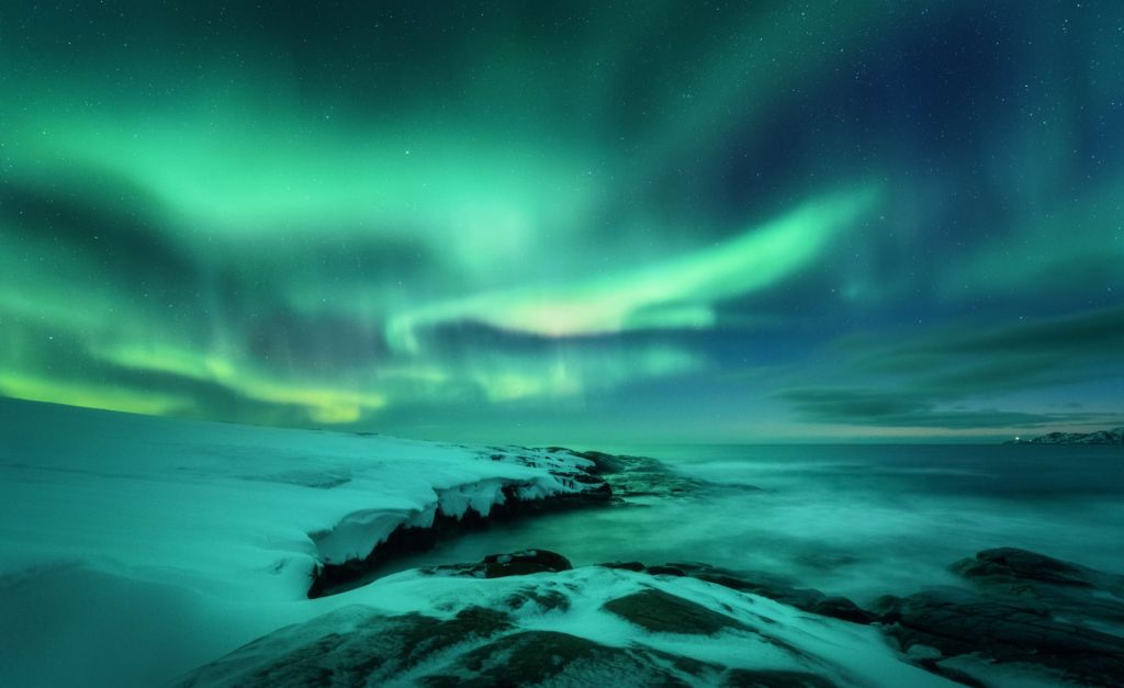 Aurora boreale verde sopra le rocce innevate