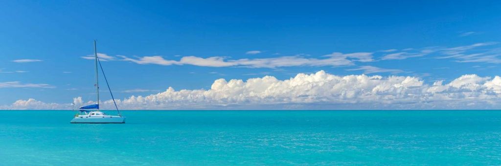 Vista panoramica di un paesaggio marino blu con barca a vela e cielo nuvoloso.