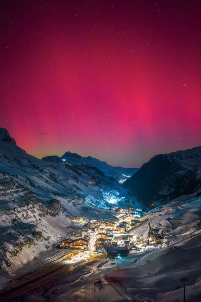 Aurora boreale rosa sopra un villaggio di montagna